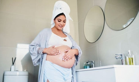 Woman applying cream to her pregnant belly at home.